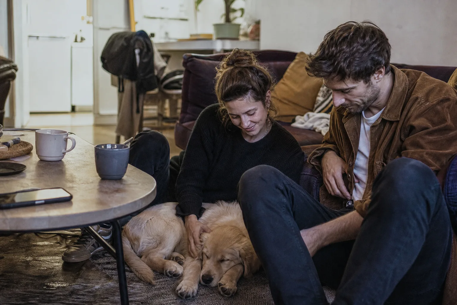 Un couple assis au sol dans son salon, un chiot golden retriever endormi sur les genoux